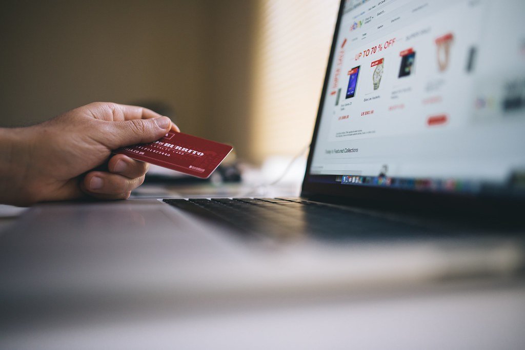 Mano sosteniendo una tarjeta de crédito roja frente a una laptop que muestra una tienda en línea